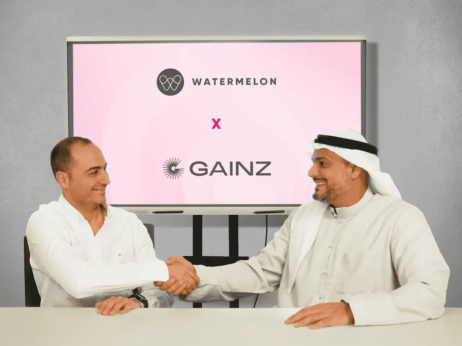 Watermelon and Gainz representatives shaking hands in front of a screen showing both company logos